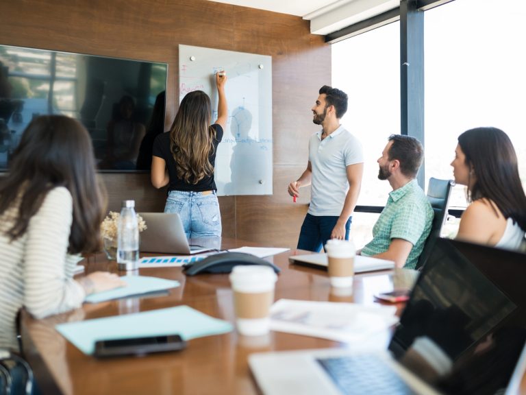 Colleagues looking at businesswoman writing on whiteboard at office during presentation