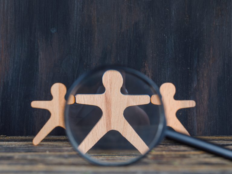 Marketing analysis concept with magnifying glass over wooden figure on wooden and grunge background close-up.